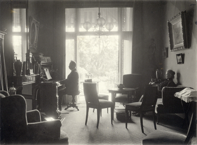 222115 Afbeelding van dr. J. Hartelust (achter de piano) en mevr. C.C. Hartelust-Schilthuis in de woonkamer van hun ...